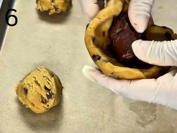 Filling cookie dough with frozen Nutella and shaping it into smooth balls.